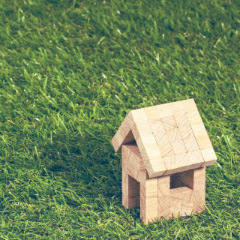Деревянная модель дома на зелёной траве.