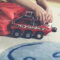 Ребёнок катает игрушечную машину на ковре.