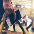 Человек несет в одной руке багаж и заграничный паспорт с вложенными в него билетами на самолёт.